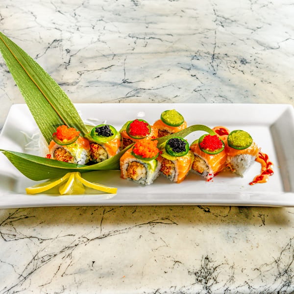 Wasabi Sushi's salmon rolls with colorful roe, jalapeños, and lemon slices on a white plate.