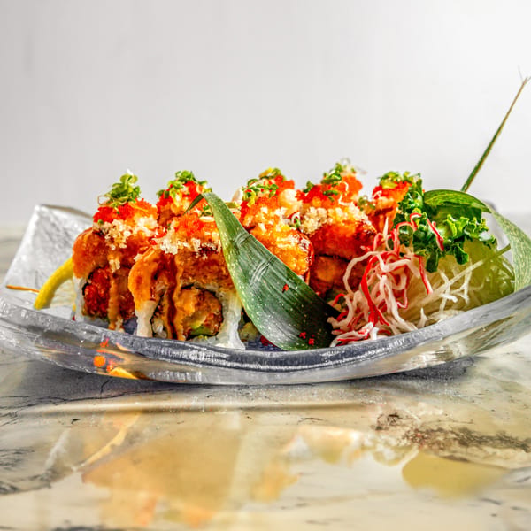 Wasabi Sushi's specialty sushi rolls, topped with orange roe, green onions, and drizzled sauce, on a clear plate.